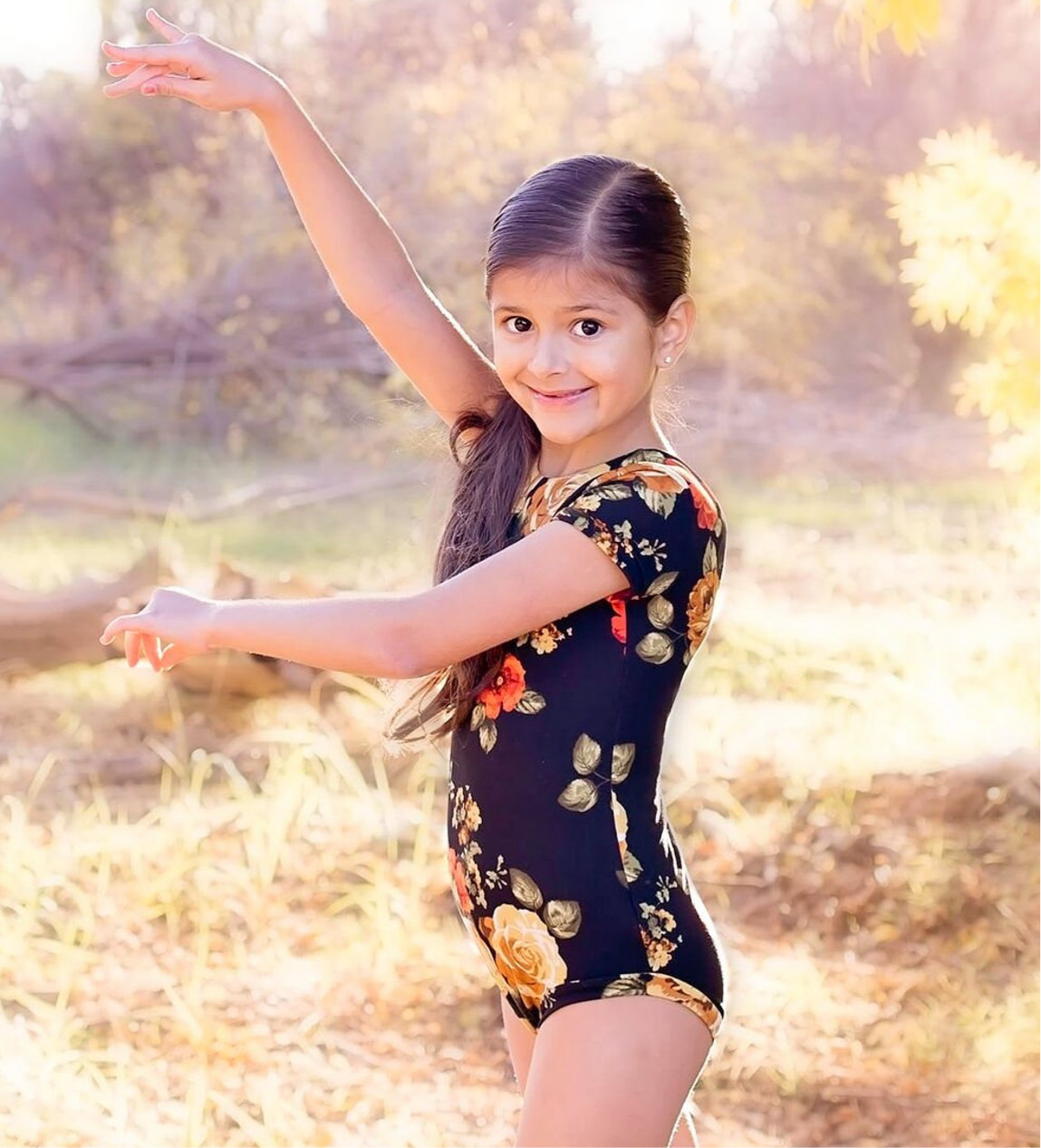Little girl wearing a black short sleeve leotard with a floral print with comfortable leg bands