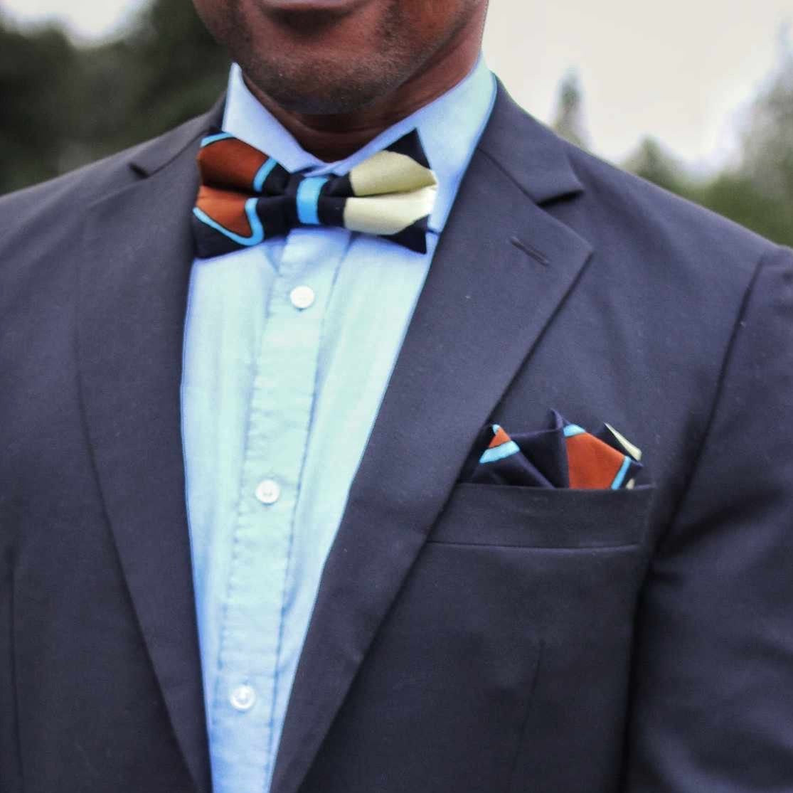 Black with brown, blue and yellow geometric design bow tie worn by an African American man in a suit.