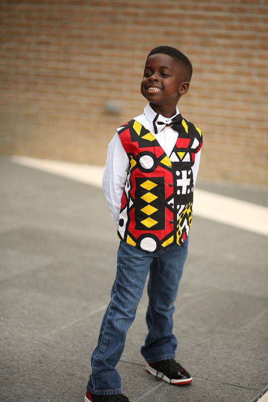 African American boy wearing an African Ankara print of red, black, yellow and white with geo,ethic shapes. The vest has black snaps or black buttons. Vest comes with coordinating bow tie of the same fabric.