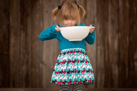 Girl wearing a blue skirt with red, whites and black dog print and holding a baking bowl