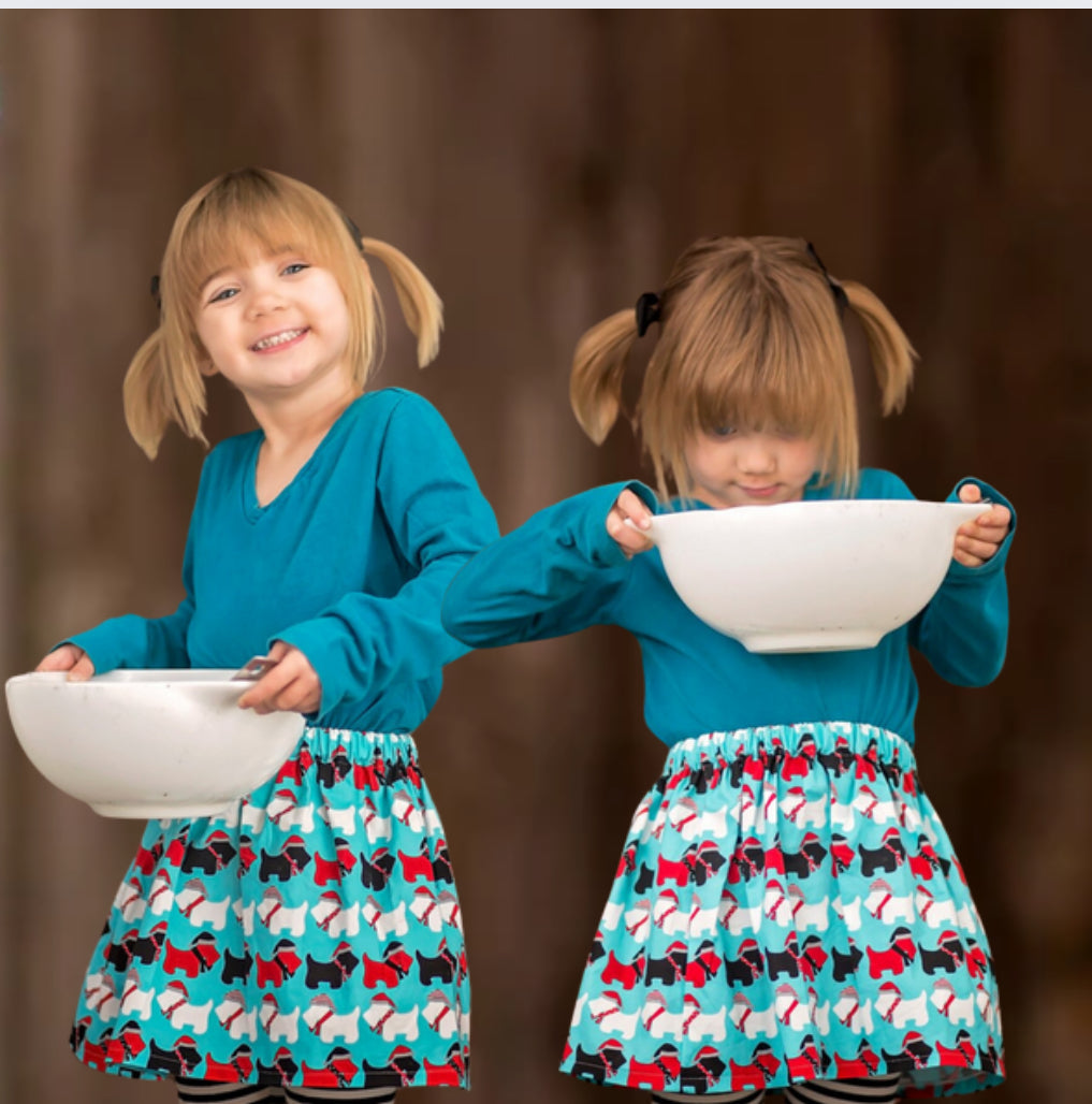 Girl wearing a blue skirt with red, whites and black dog print and holding a baking bowl
