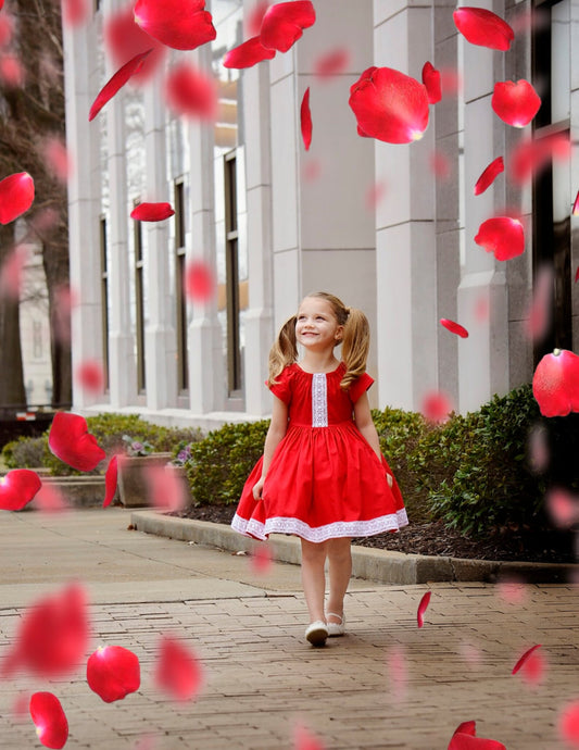 Little girl wearing a red peasant dress suitable for Christmas or Valentine’s Day with white lace trim