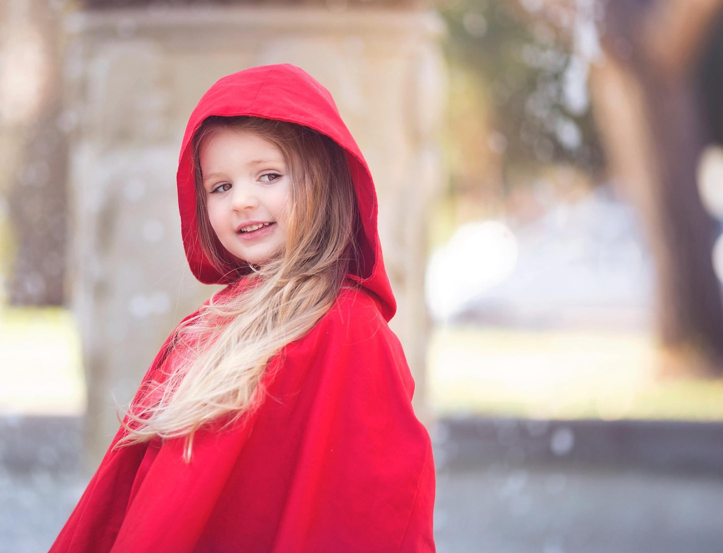 Girl dressed as Red Riding Hood wearing a red cape with oversized hood as a Halloween or party costume