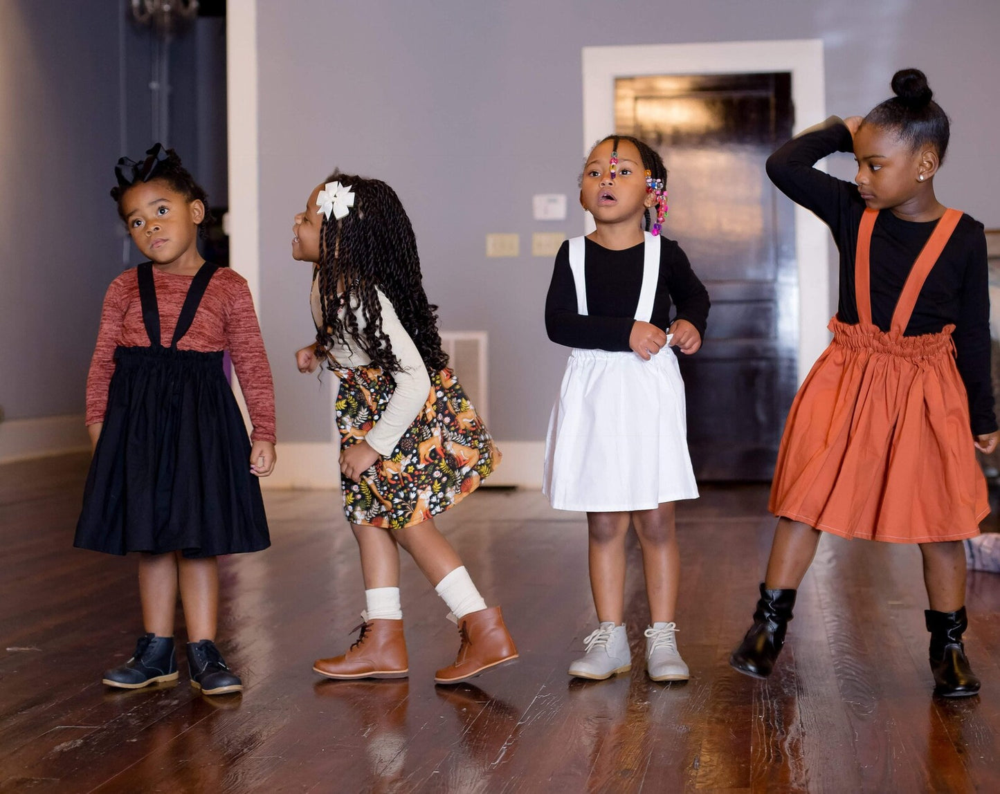 Four young girls in stylish suspender skirt standing on a wooden floor.