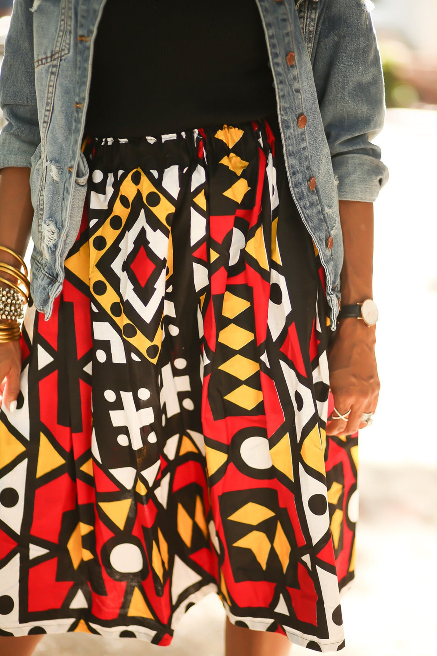 Close up view of the skirt of an African American woman wearing an African print, red, black, yellow and white geometric print skirt.