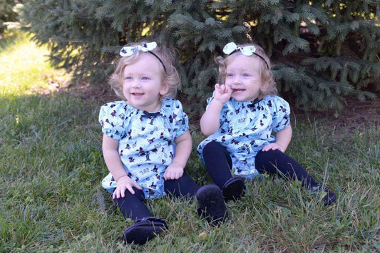 Alice in Wonderland Romper in Blue and White prints. Scenes depicted from Alice in Wonderland on this cotton fabric. The baby romper is a peasant neckline with elastic sleeves and snaps at the crotch of the romper.