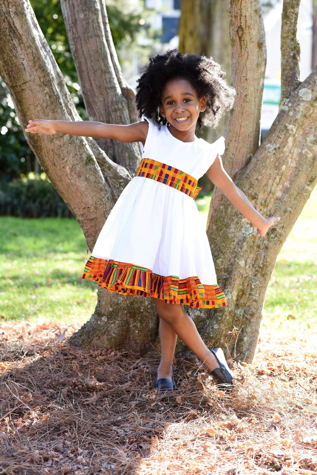 African American girl about 8 years old wearing a short sleeve white dress with orange geometric print hem and waistband. 