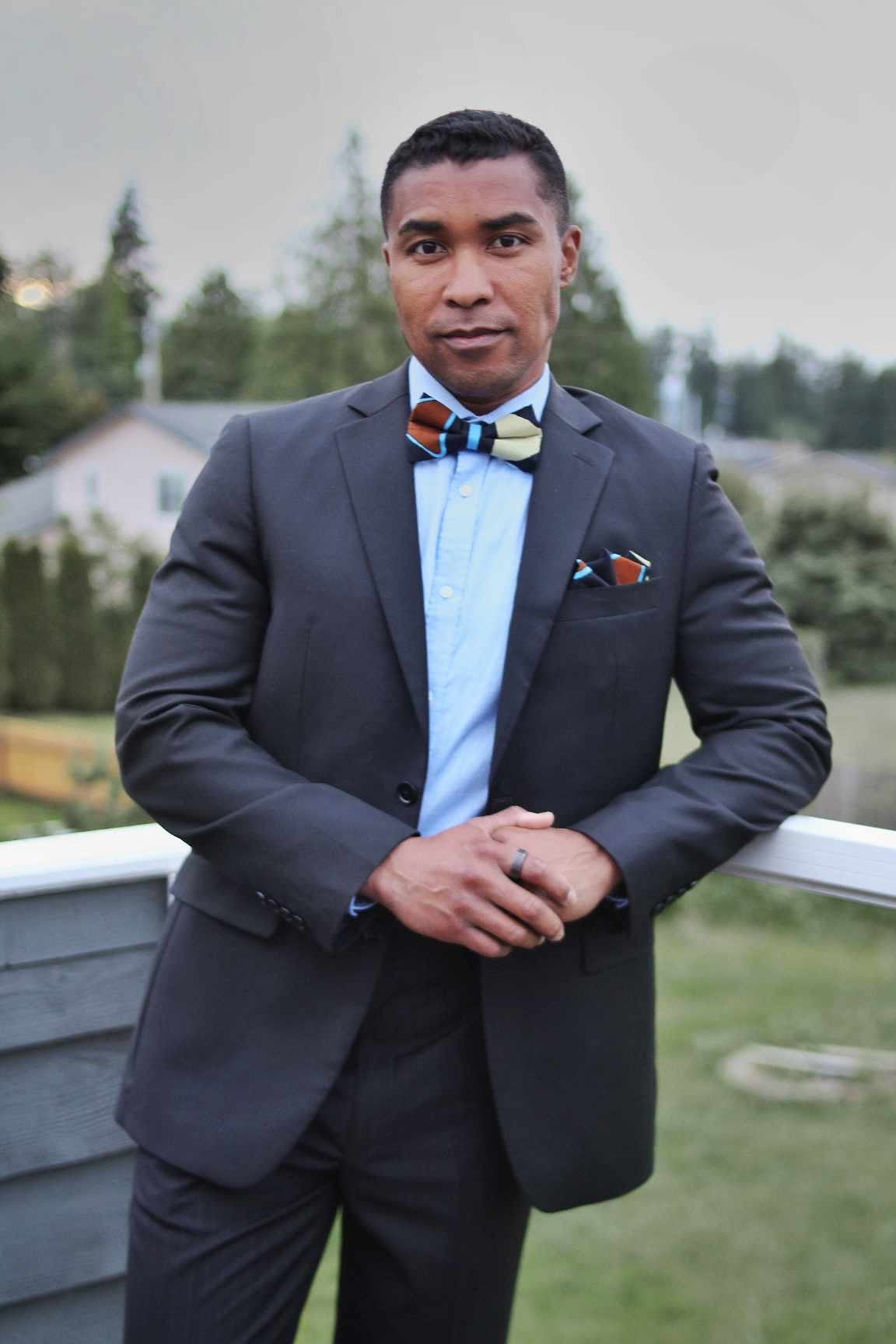 Black with brown, blue and yellow geometric design bow tie worn by an African American man in a suit.