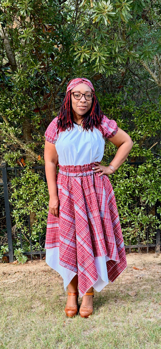 Jamaican woman in red, white, and blue plaid bandana skirt set with peasant blouse, handkerchief hem double layer skirt, and twisted knot headband.