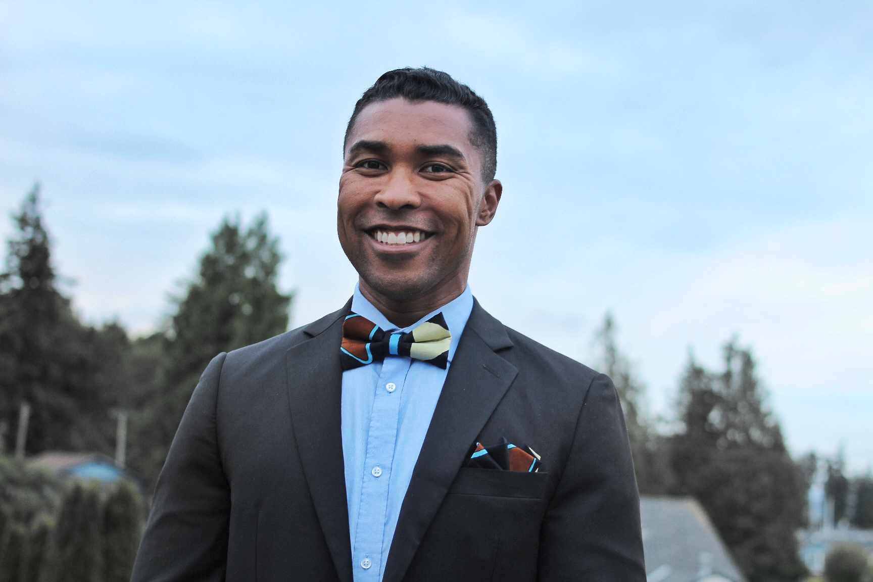 Black with brown, blue and yellow geometric design bow tie worn by an African American man in a suit.