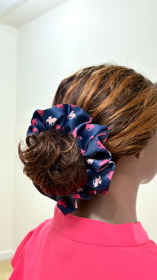 Back view of a mannequin in a pink top wearing hair in a low ponytail  bun wearing a jumbo horse print navy with fuchsia and light pink horses satin scrunchie 