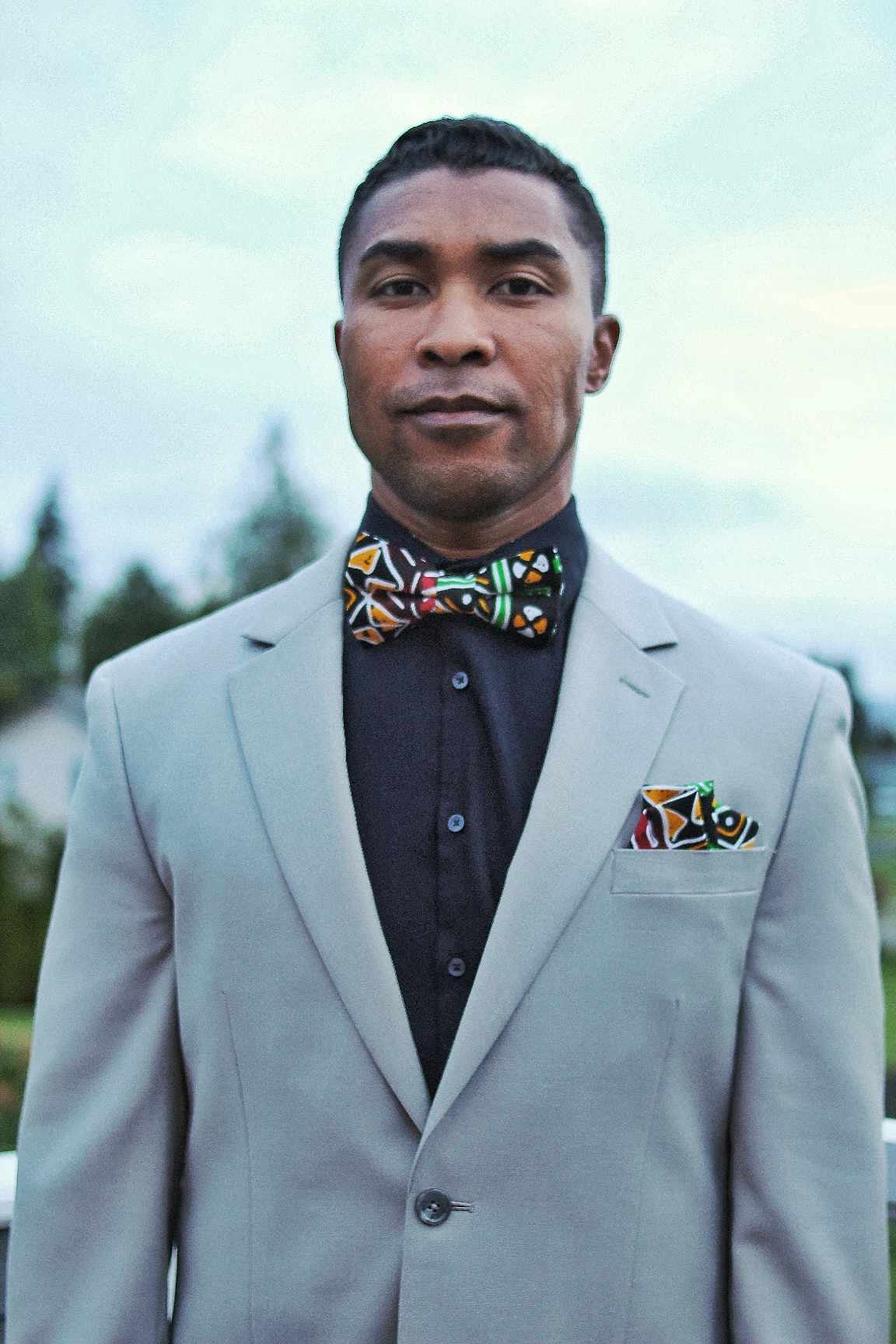 African American man wearing a grey suit and is wearing our Black multi color Reggae bow tie and pocket square