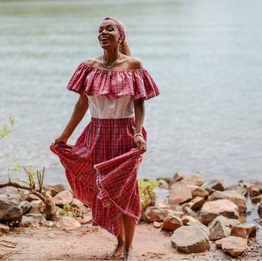 Jamaican lady wearing a traditional bandana red plaid print skirt and white and bandana print top with a headwrap