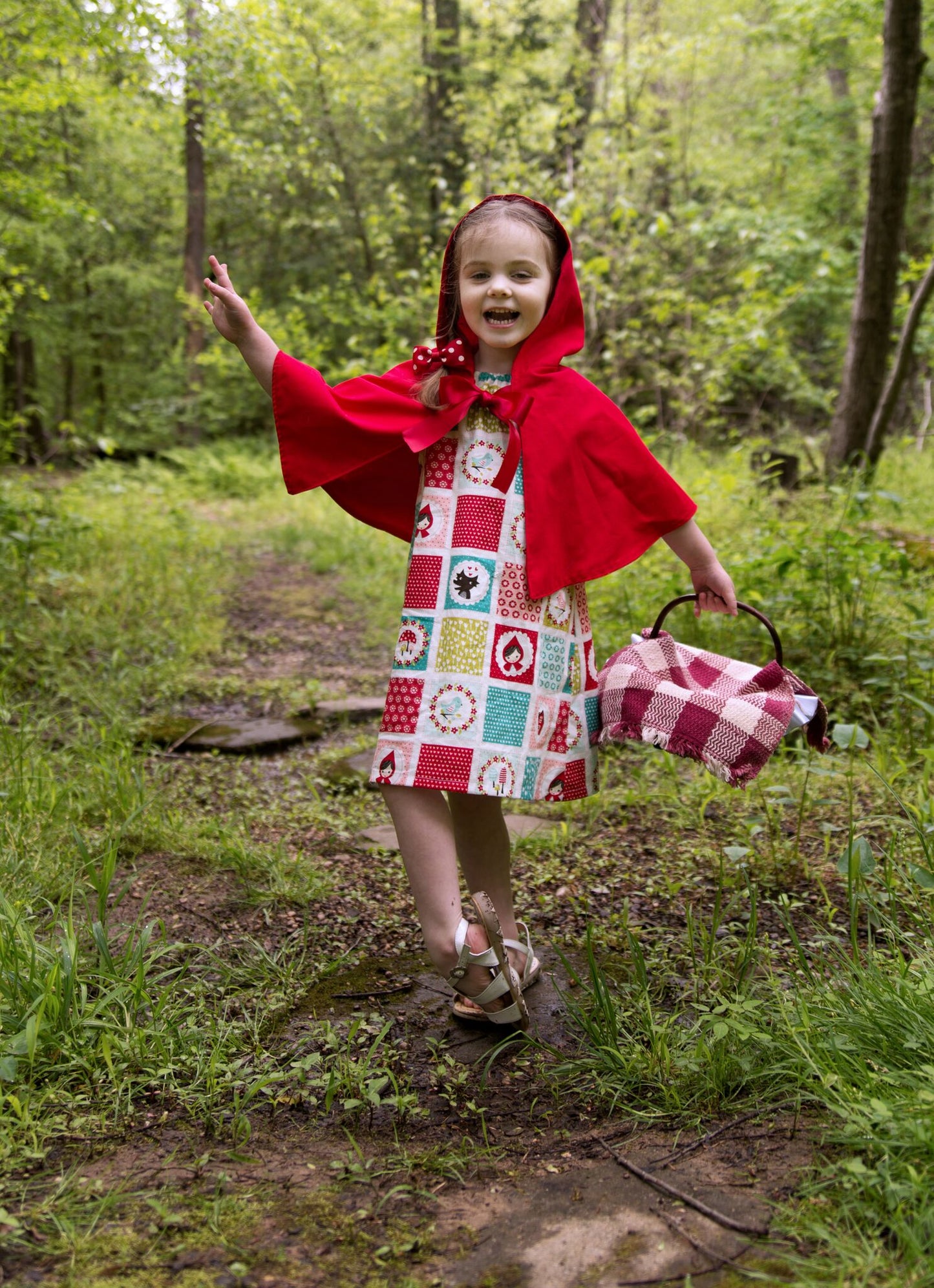 Girl wearing a Red Riding Hood character print peasant dress with red hooded cape.