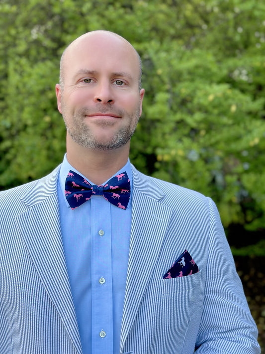 A man wearing a blue striped suit and a navy bow tie with a horse pattern.