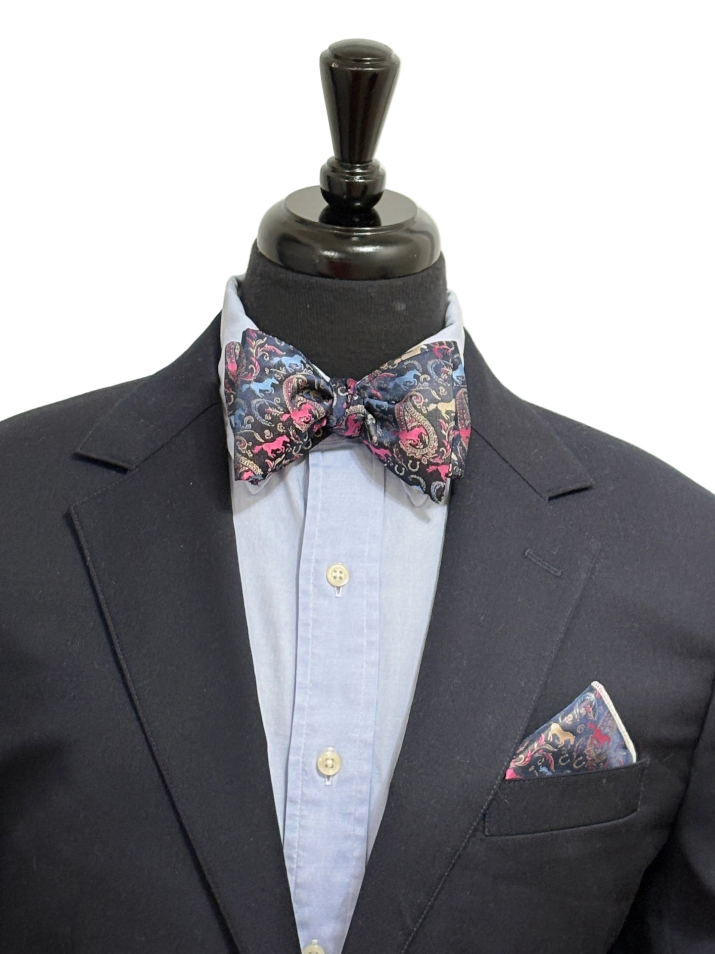 Black suit with a paisley horse theme patterned self tied bow tie and pocket square on a mannequin against a white background