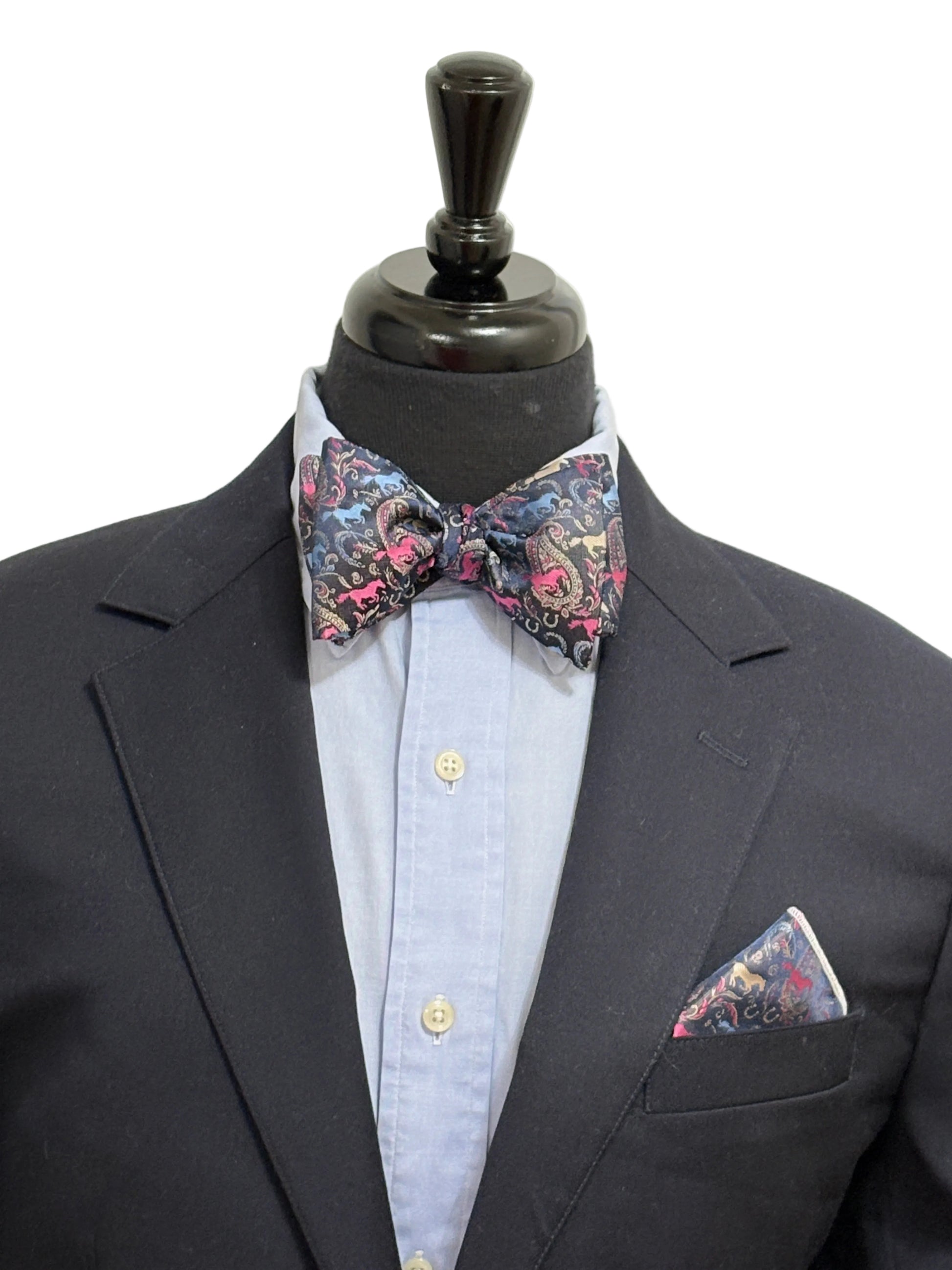 Black suit with a paisley horse theme patterned self tied bow tie and pocket square on a mannequin against a white background