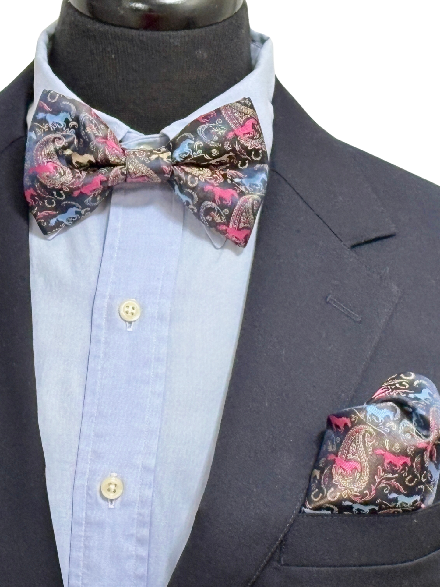 Paisley patterned navy with fuchsia and blue bow tie and pocket square on a mannequin with a light blue shirt and dark suit.