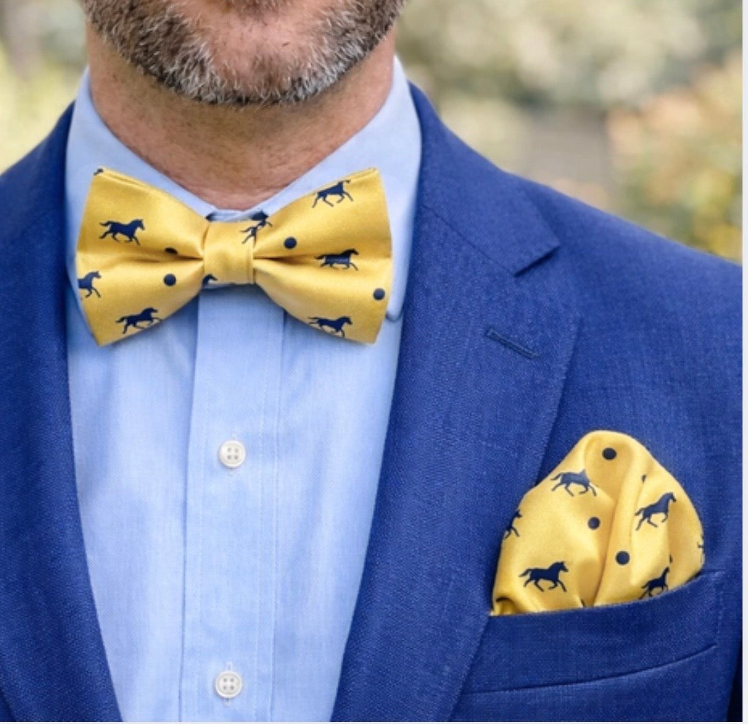 Man wearing a blue suit with a yellow bow tie and pocket square featuring horse patterns.