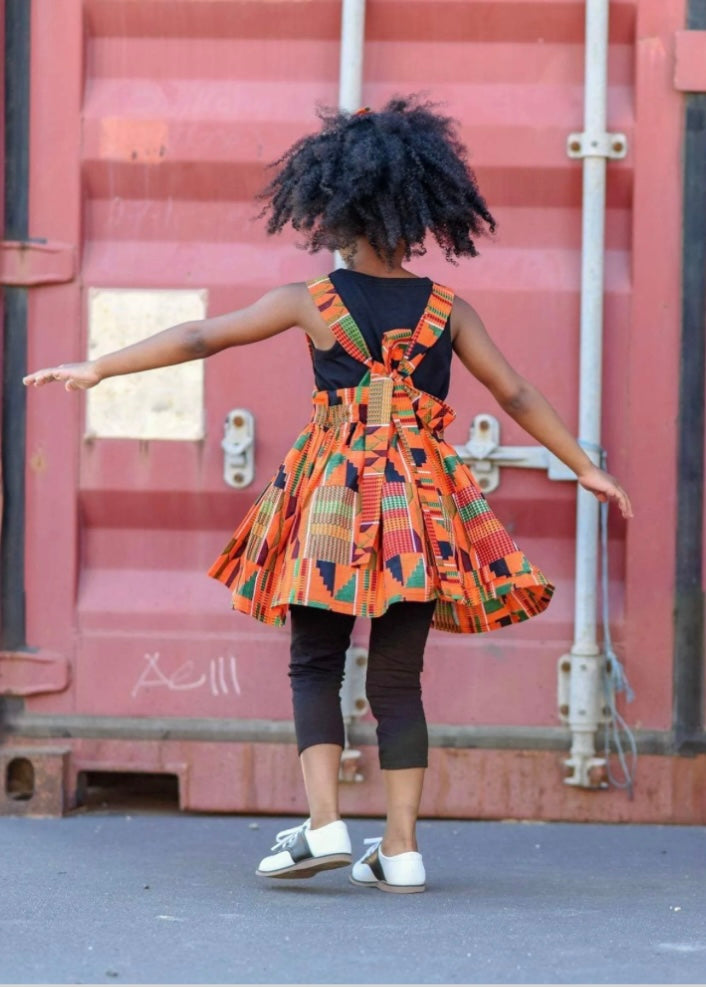 Back view of African American girl wearing orange Kente suspender skirt.