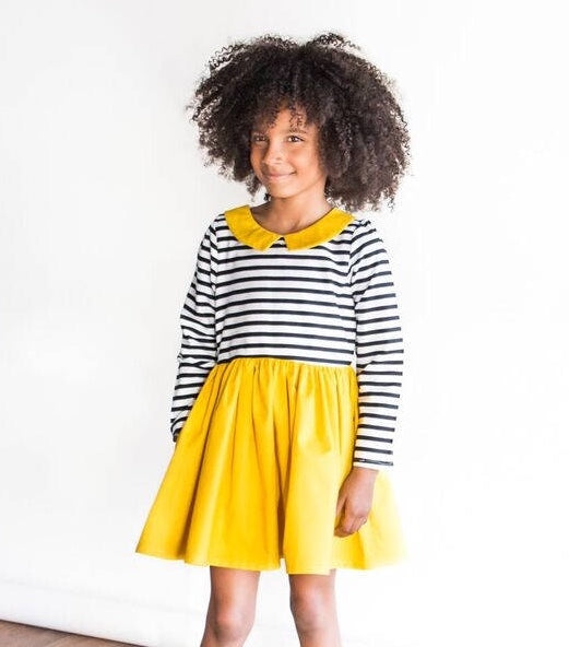 Little girl wearing a girl’s mustard yellow Dress with Black and White Striped Bodice and a mustard yellow collar.