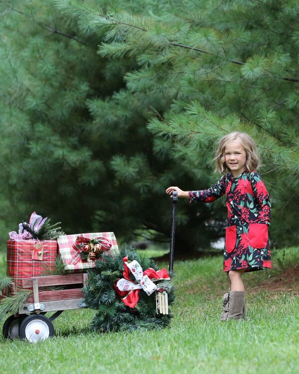 Girl wearing a black poinsettia print dress with red pockets. 