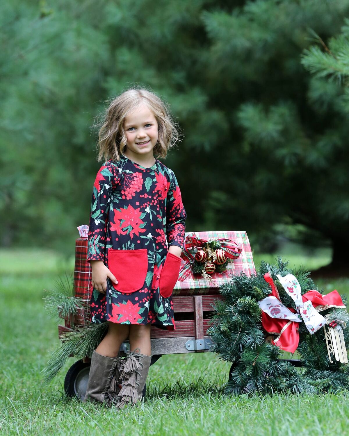 Little girl wearing a black knit dress with red poinsettias print and red pockets. 