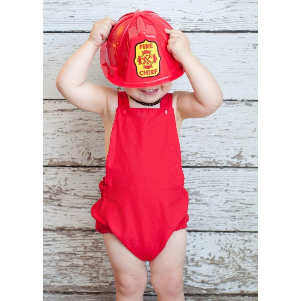 Little boy in a red boho baby romper and a red fire chief play hat