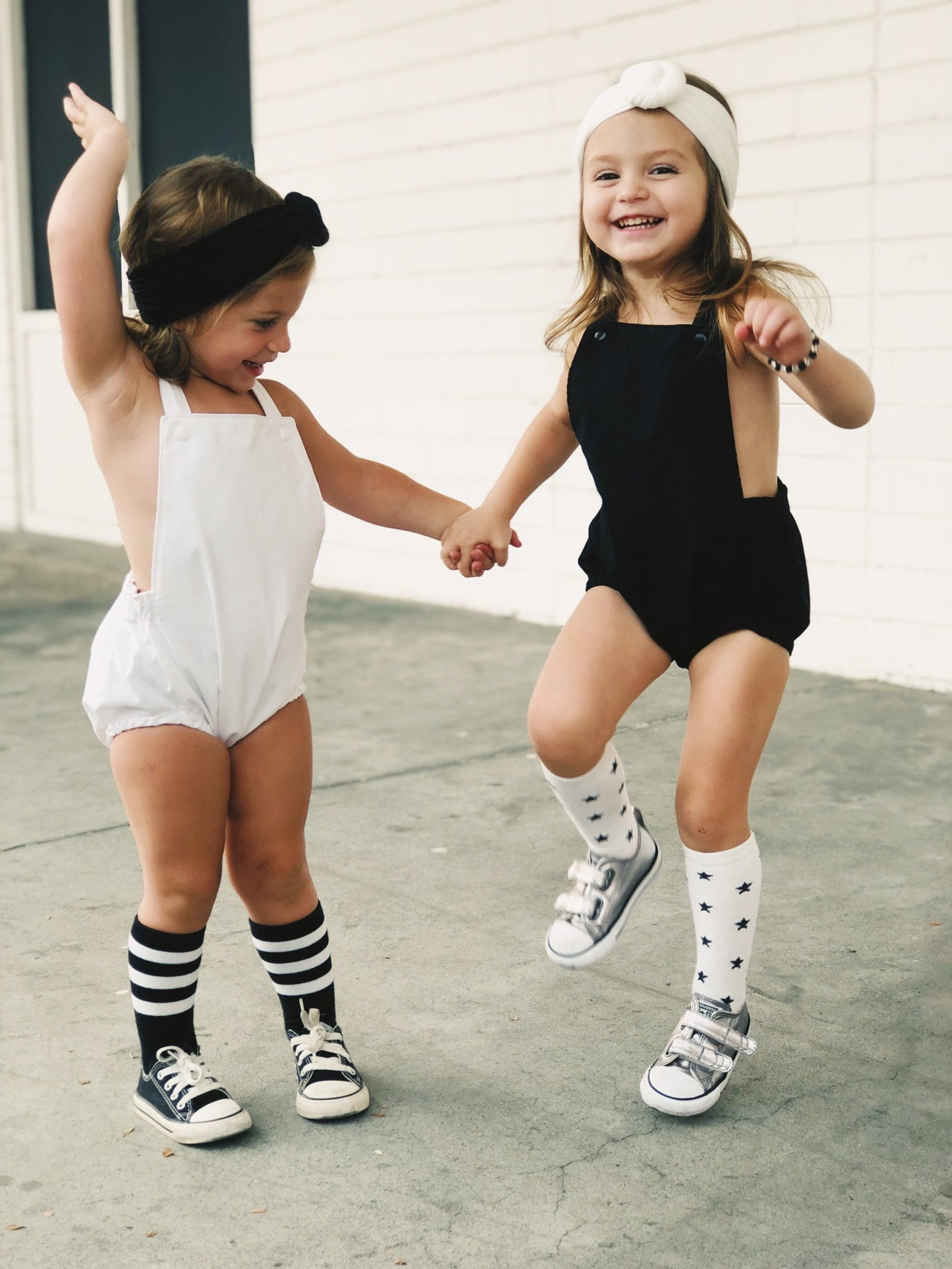 Little girls dancing in their boho sleeveless cross back style black romper and white rompers